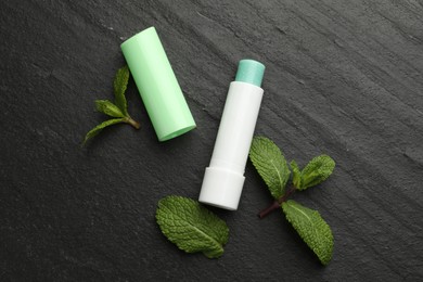 Photo of Mint lip balm and green leaves on black table, flat lay. Cosmetic product