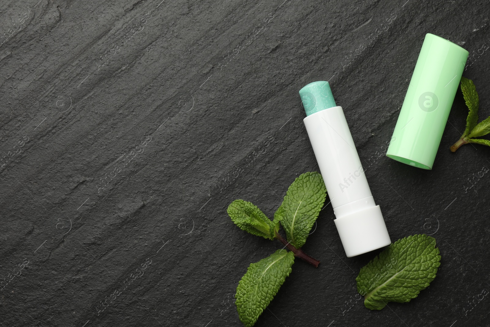 Photo of Mint lip balm and green leaves on black background, flat lay. Space for text