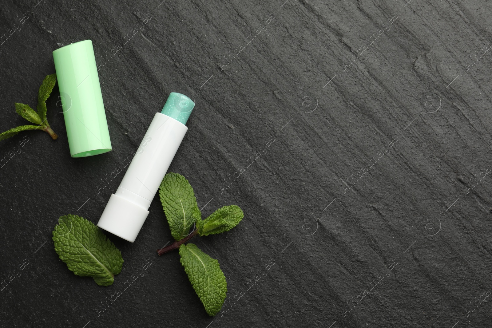 Photo of Mint lip balm and green leaves on black background, flat lay. Space for text