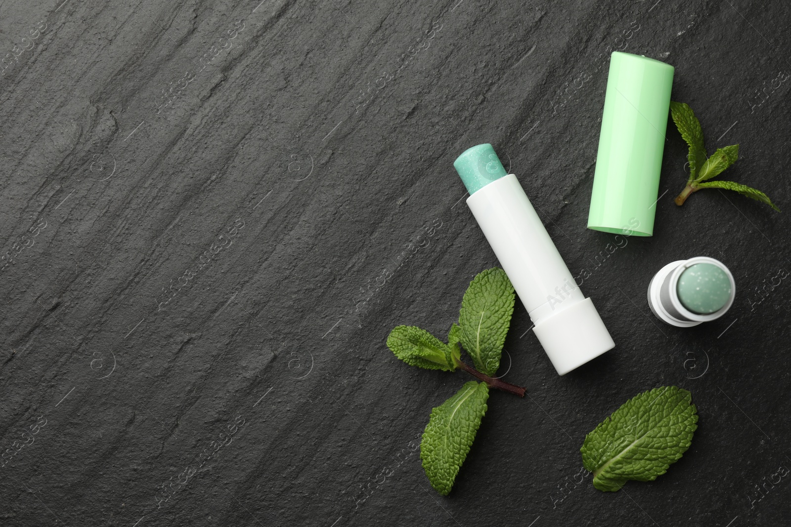 Photo of Mint lip balms and green leaves on black background, flat lay. Space for text