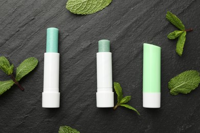 Photo of Mint lip balms and green leaves on black table, flat lay. Cosmetic product