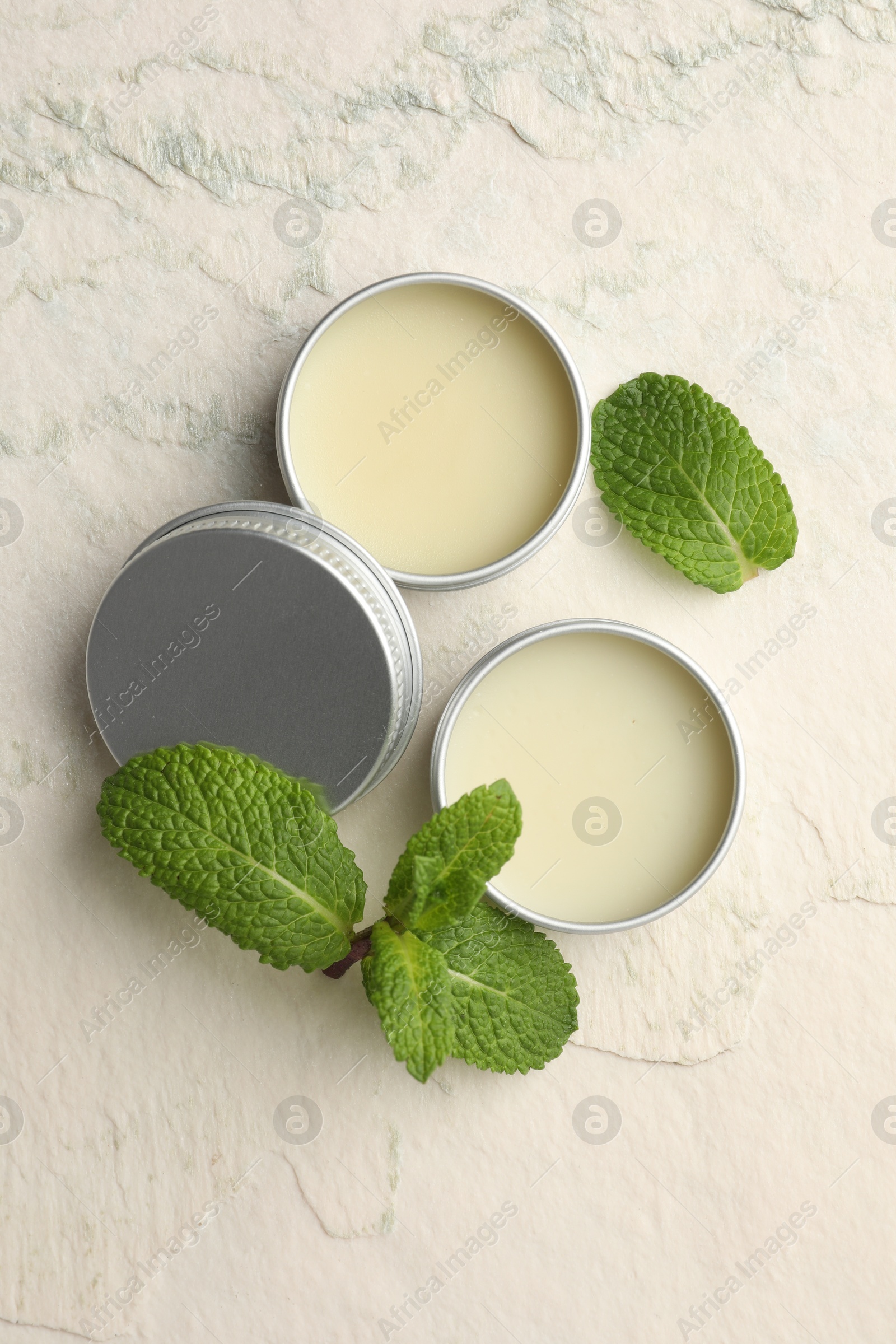 Photo of Mint lip balms and green leaves on beige textured table, flat lay. Cosmetic product