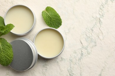 Photo of Mint lip balms and green leaves on beige textured background, flat lay. Space for text