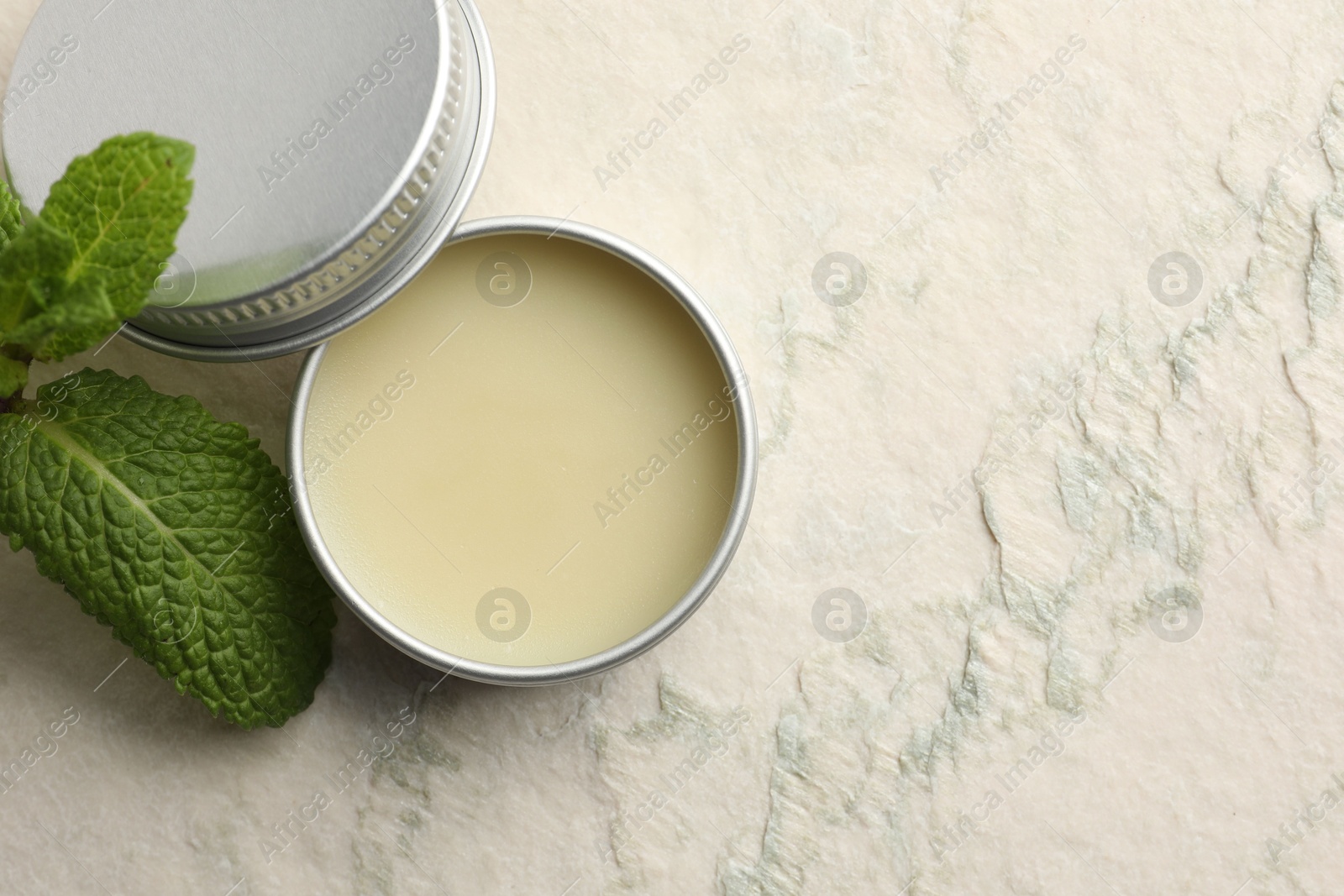 Photo of Mint lip balm and green leaves on beige textured background, top view. Space for text