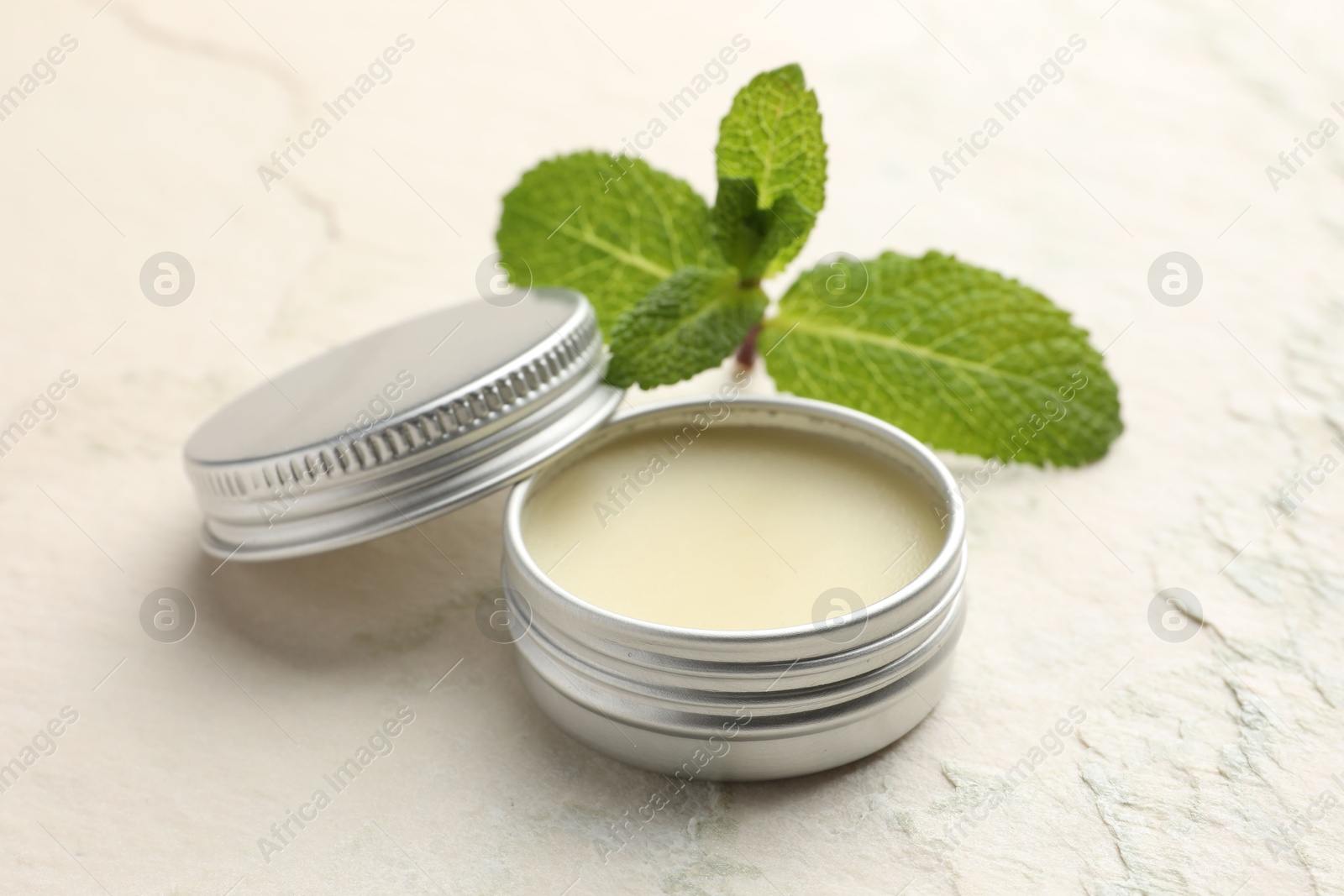 Photo of Mint lip balm and green leaves on beige textured table, closeup. Cosmetic product