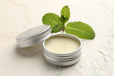 Photo of Mint lip balm and green leaves on beige textured table, closeup. Cosmetic product