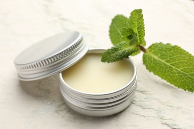 Photo of Mint lip balm and green leaves on beige textured table, closeup. Cosmetic product