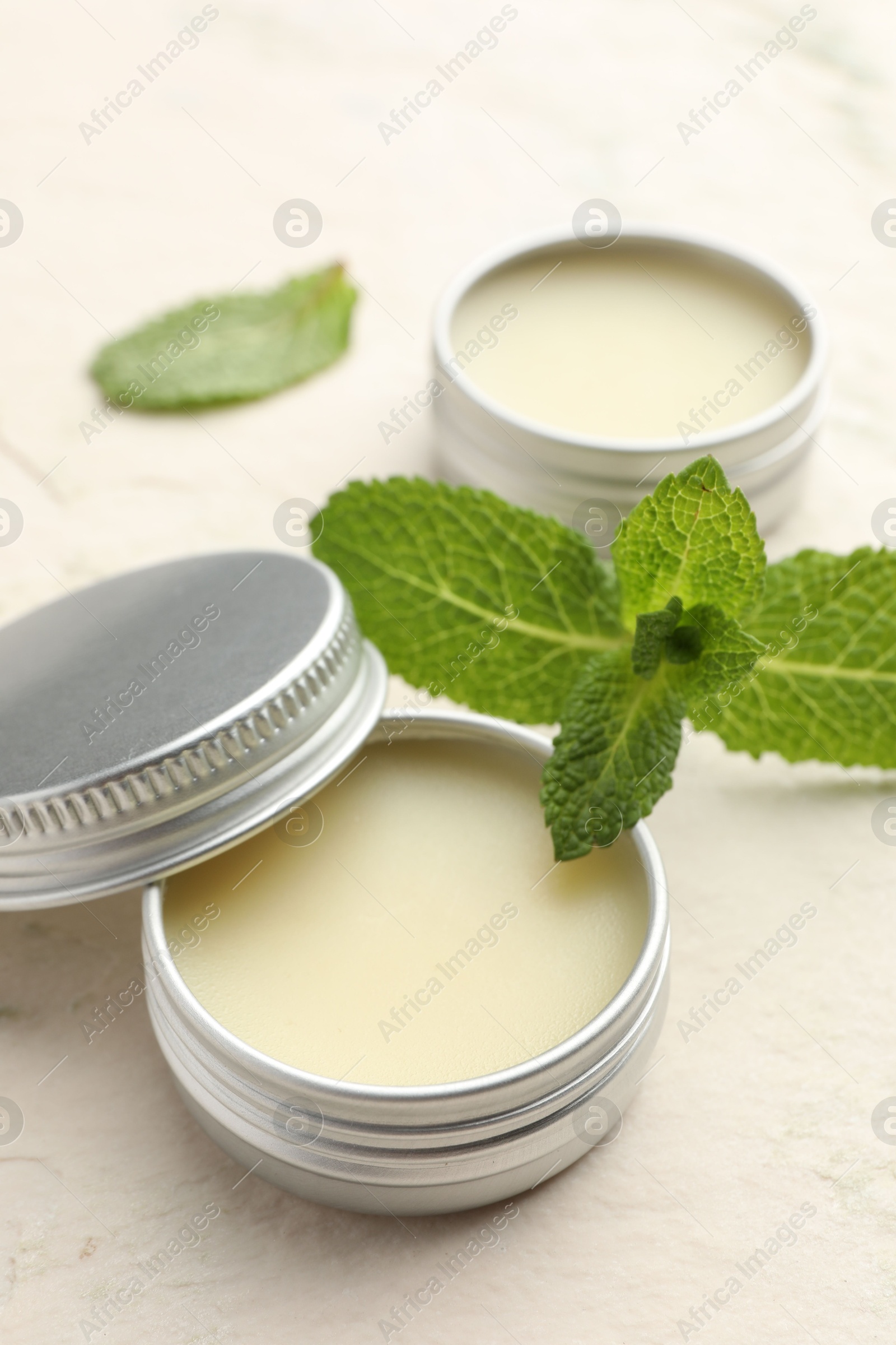 Photo of Mint lip balms and green leaves on beige textured table, closeup. Cosmetic product