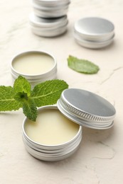 Photo of Mint lip balms and green leaves on beige textured table, closeup. Cosmetic product