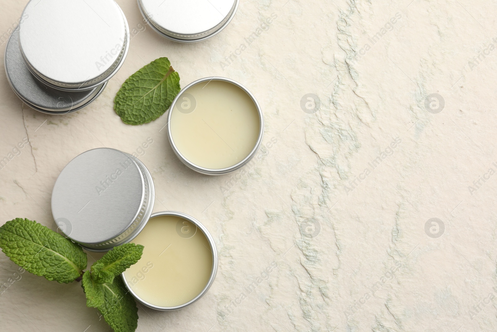 Photo of Mint lip balms and green leaves on beige textured background, flat lay. Space for text