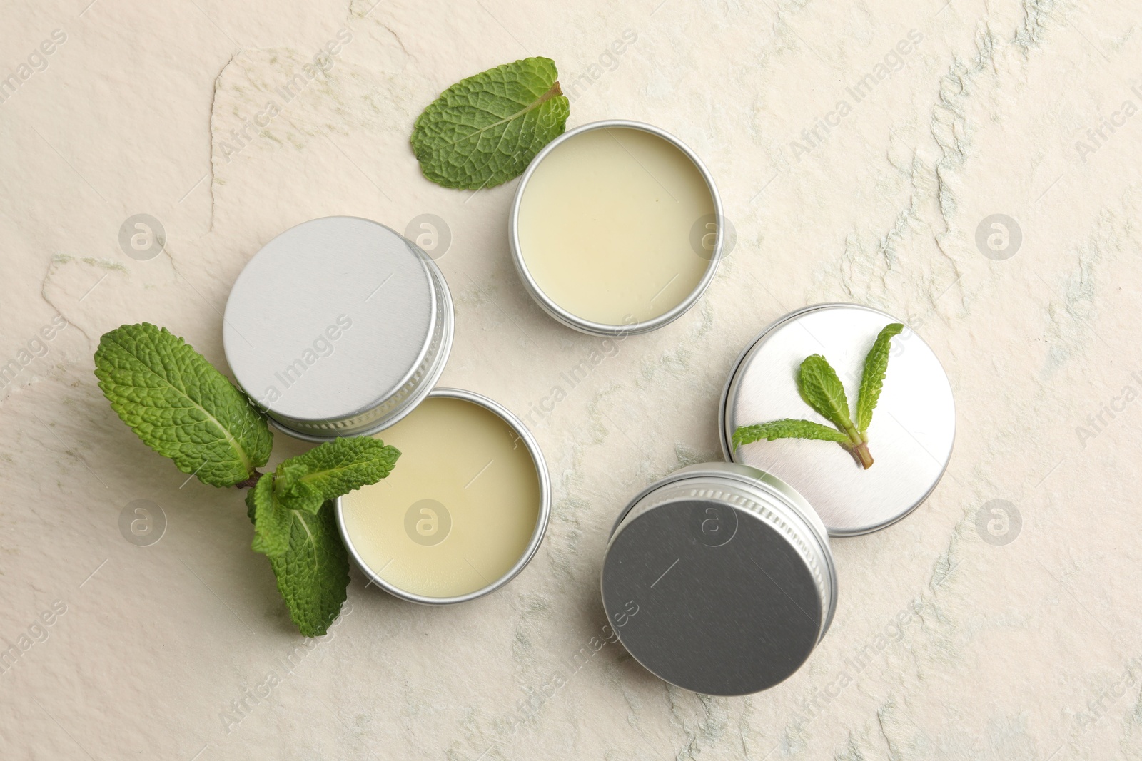 Photo of Mint lip balms and green leaves on beige textured background, flat lay. Cosmetic product