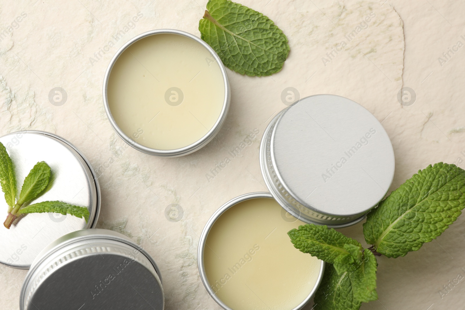 Photo of Mint lip balms and green leaves on beige textured background, flat lay. Cosmetic product