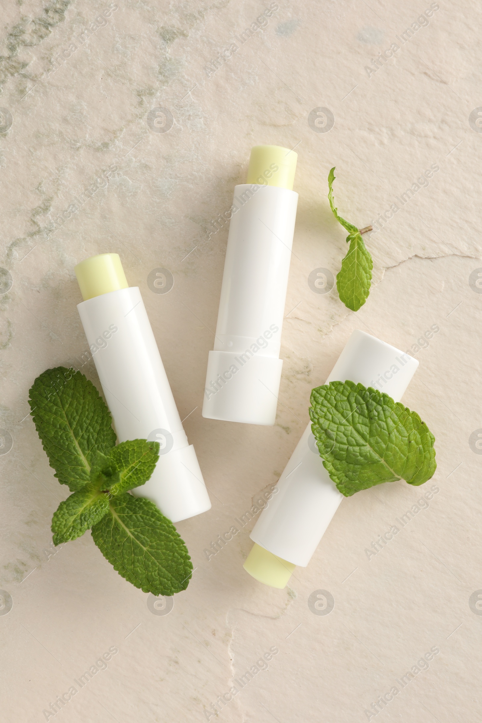 Photo of Mint lip balms and green leaves on beige textured background, flat lay. Cosmetic product