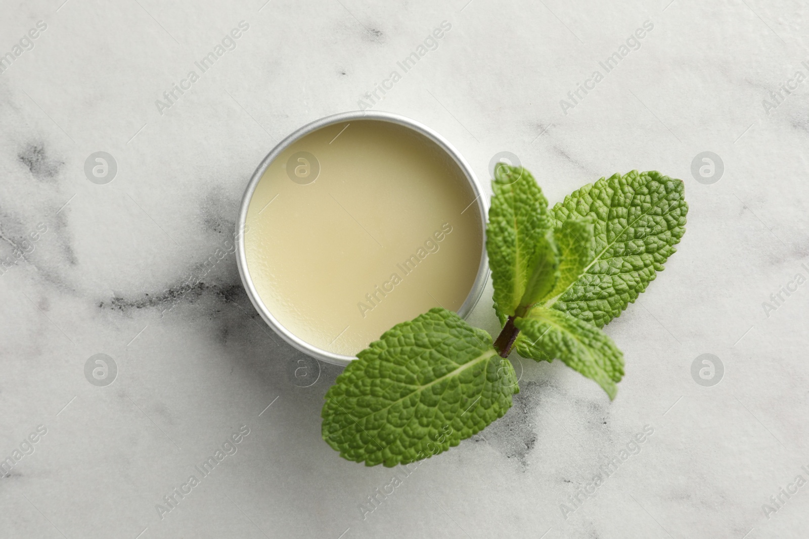 Photo of Mint lip balm and green leaves on white marble table, top view. Cosmetic product