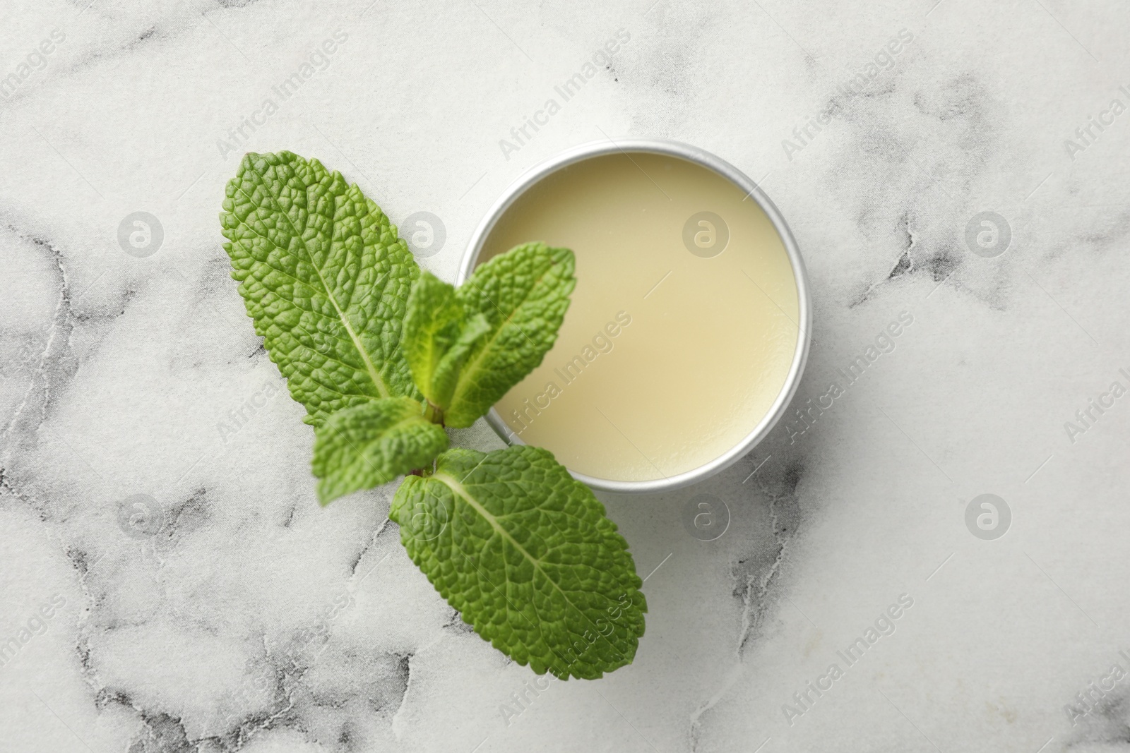 Photo of Mint lip balm and green leaves on white marble table, top view. Cosmetic product