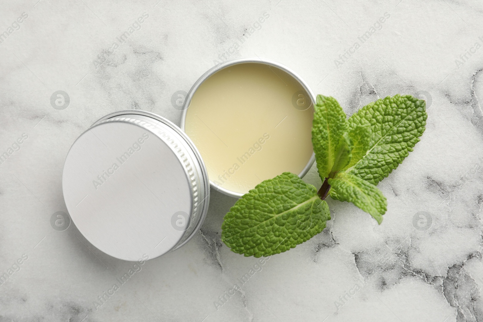 Photo of Mint lip balm and green leaves on white marble background, top view. Cosmetic product