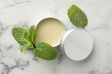 Photo of Mint lip balm and green leaves on white marble background, top view. Cosmetic product