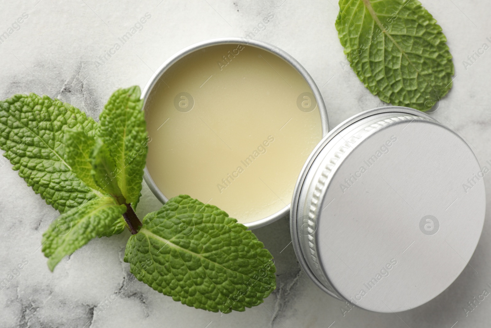 Photo of Mint lip balm and green leaves on white marble background, top view. Cosmetic product