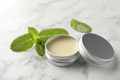 Photo of Mint lip balm and green leaves on white marble table, closeup. Cosmetic product