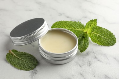 Photo of Mint lip balm and green leaves on white marble table, closeup. Cosmetic product