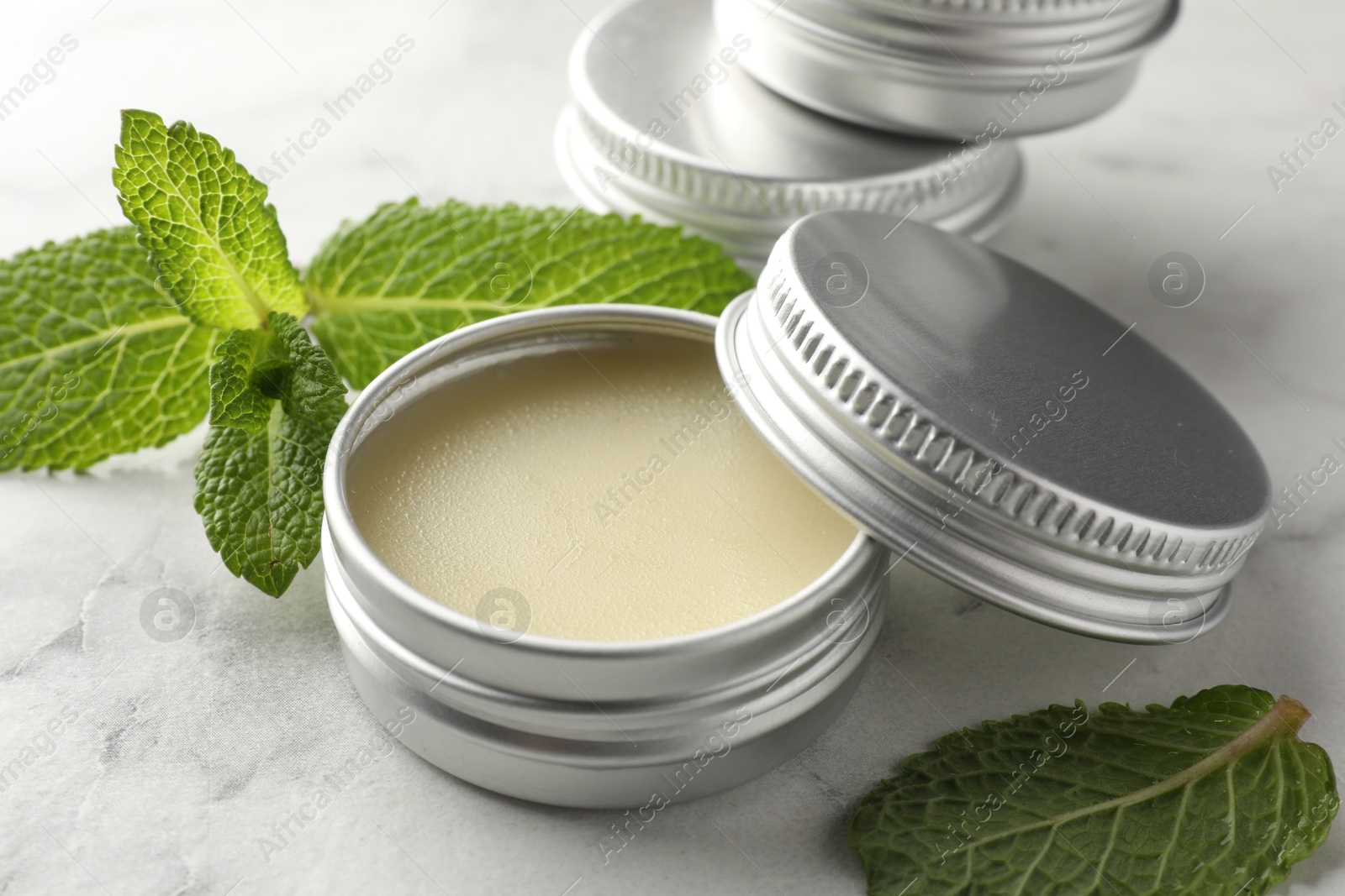 Photo of Mint lip balms and green leaves on white marble table, closeup. Cosmetic product