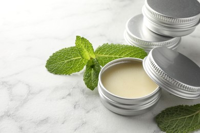 Photo of Mint lip balms and green leaves on white marble table, closeup. Cosmetic product