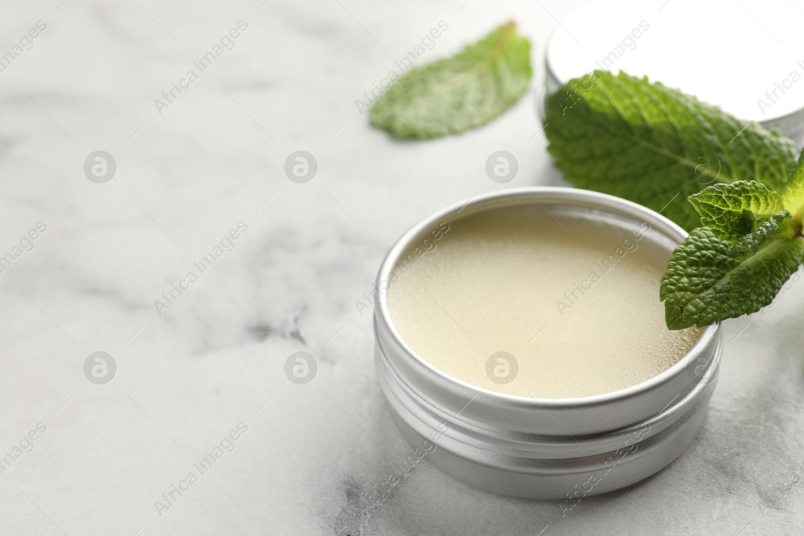 Photo of Mint lip balm and green leaves on white marble table, closeup. Space for text