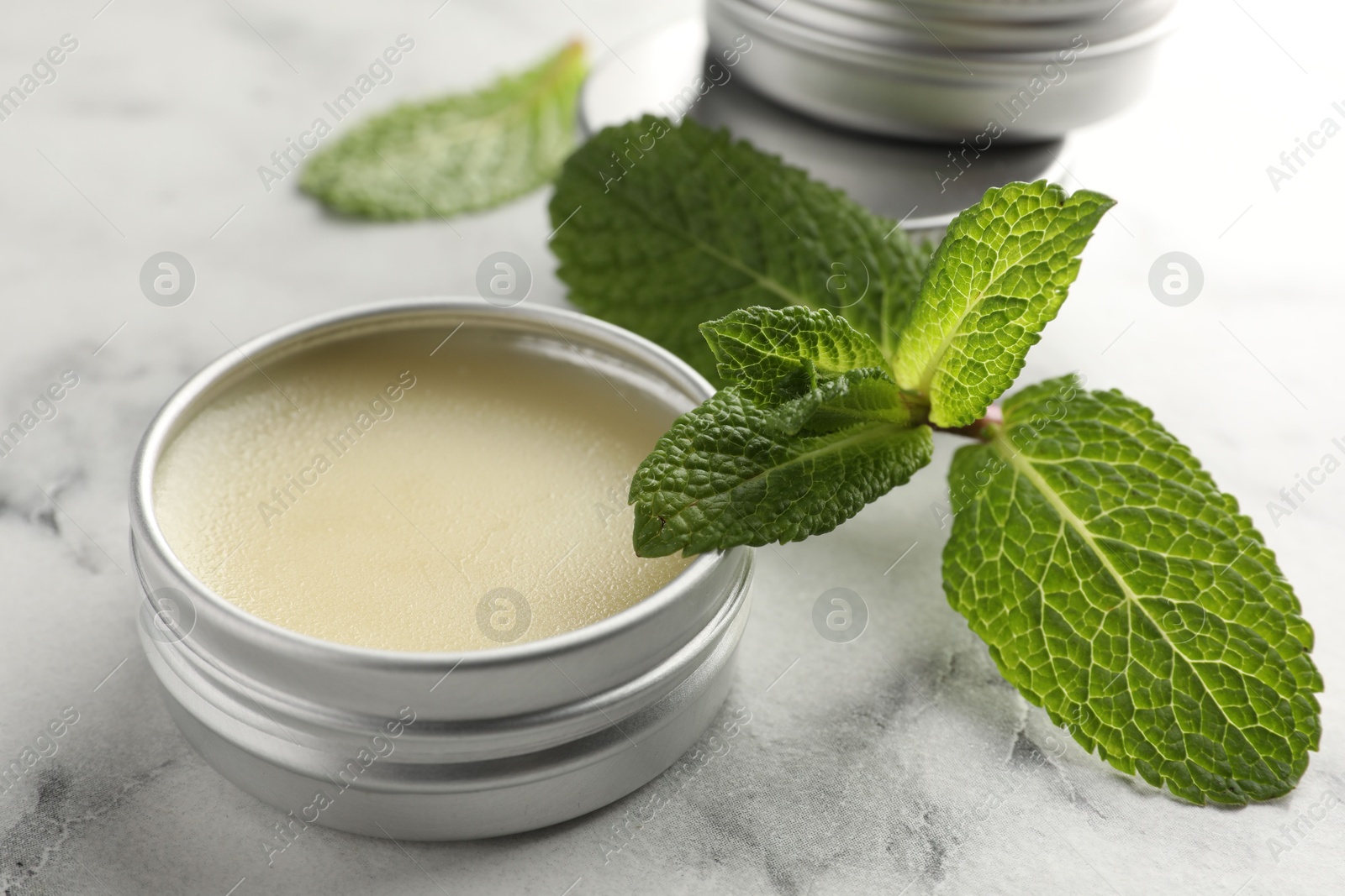 Photo of Mint lip balms and green leaves on white marble table, closeup. Cosmetic product