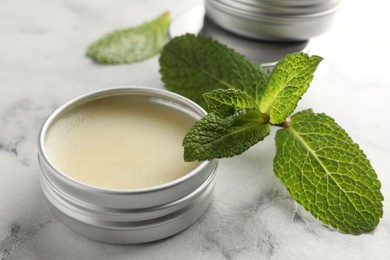 Photo of Mint lip balms and green leaves on white marble table, closeup. Cosmetic product