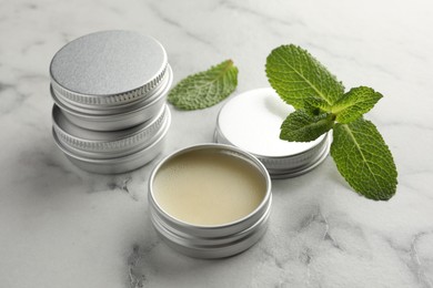 Photo of Mint lip balms and green leaves on white marble table, closeup. Cosmetic product