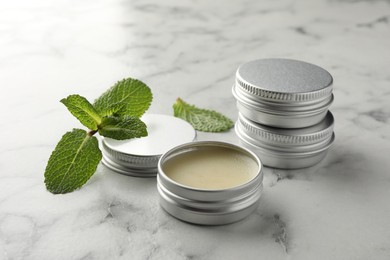 Photo of Mint lip balms and green leaves on white marble table, closeup. Cosmetic product