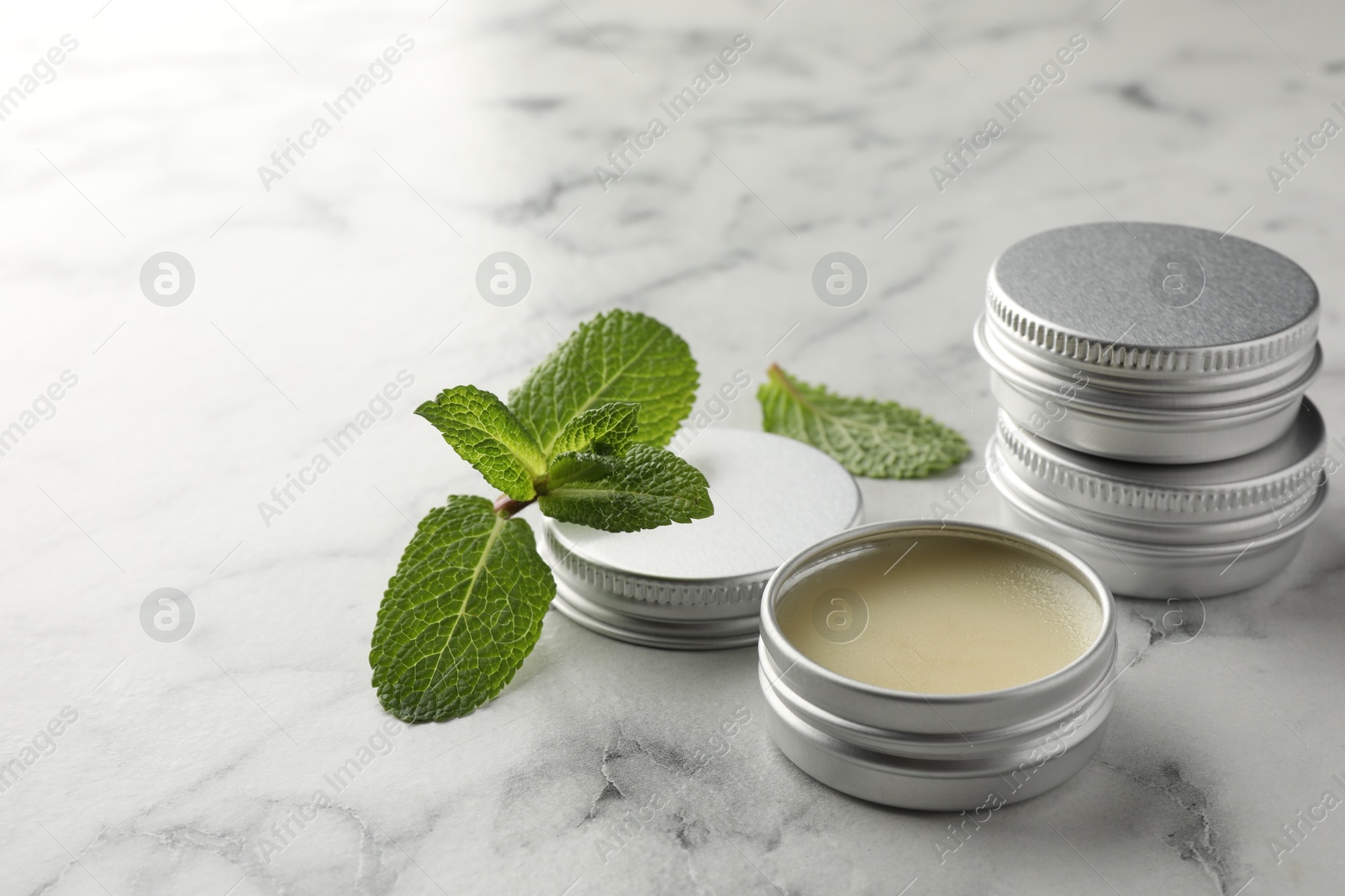 Photo of Mint lip balms and green leaves on white marble table, closeup. Cosmetic product