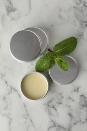 Photo of Mint lip balms and green leaves on white marble background, flat lay. Cosmetic product