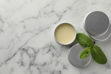 Photo of Mint lip balms and green leaves on white marble background, flat lay. Space for text