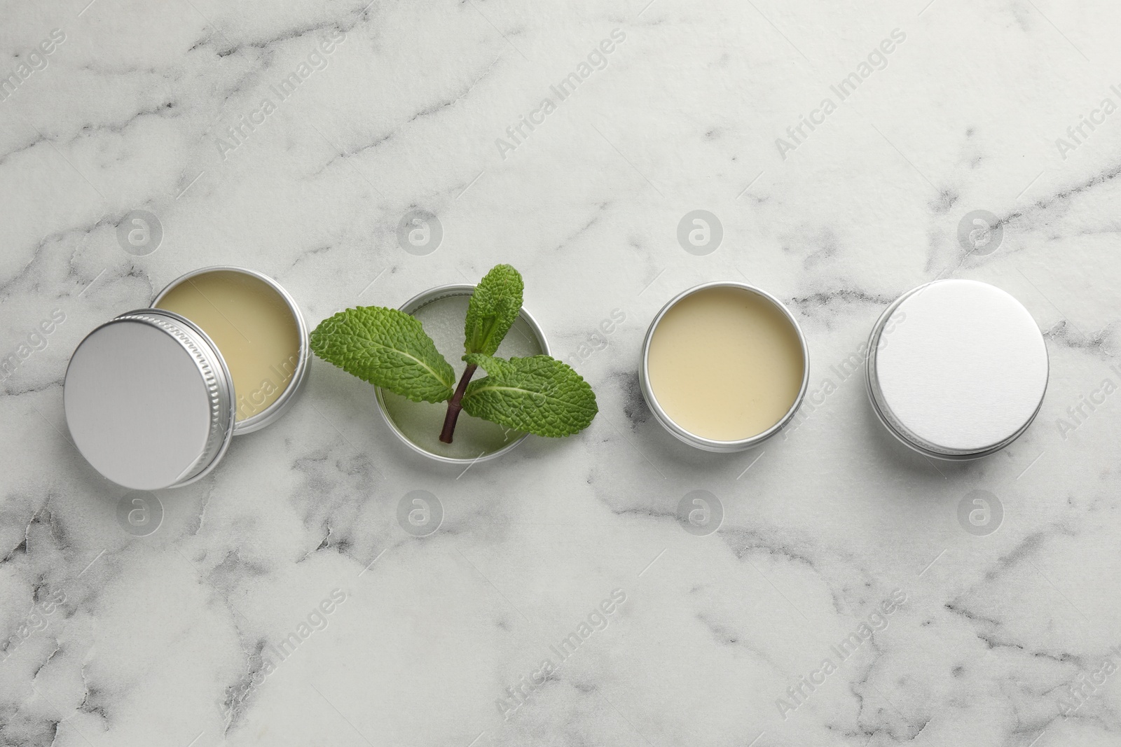 Photo of Mint lip balms and green leaves on white marble background, flat lay. Cosmetic product