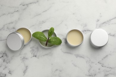 Photo of Mint lip balms and green leaves on white marble background, flat lay. Cosmetic product