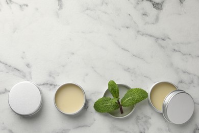 Photo of Mint lip balms and green leaves on white marble background, flat lay. Space for text