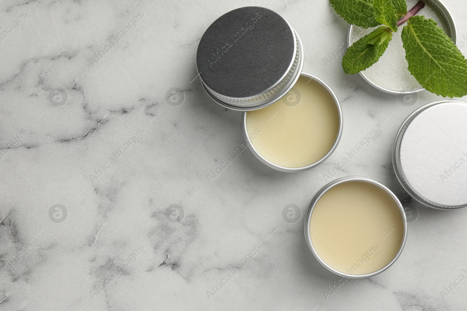 Photo of Mint lip balms and green leaves on white marble background, flat lay. Space for text