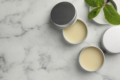 Photo of Mint lip balms and green leaves on white marble background, flat lay. Space for text