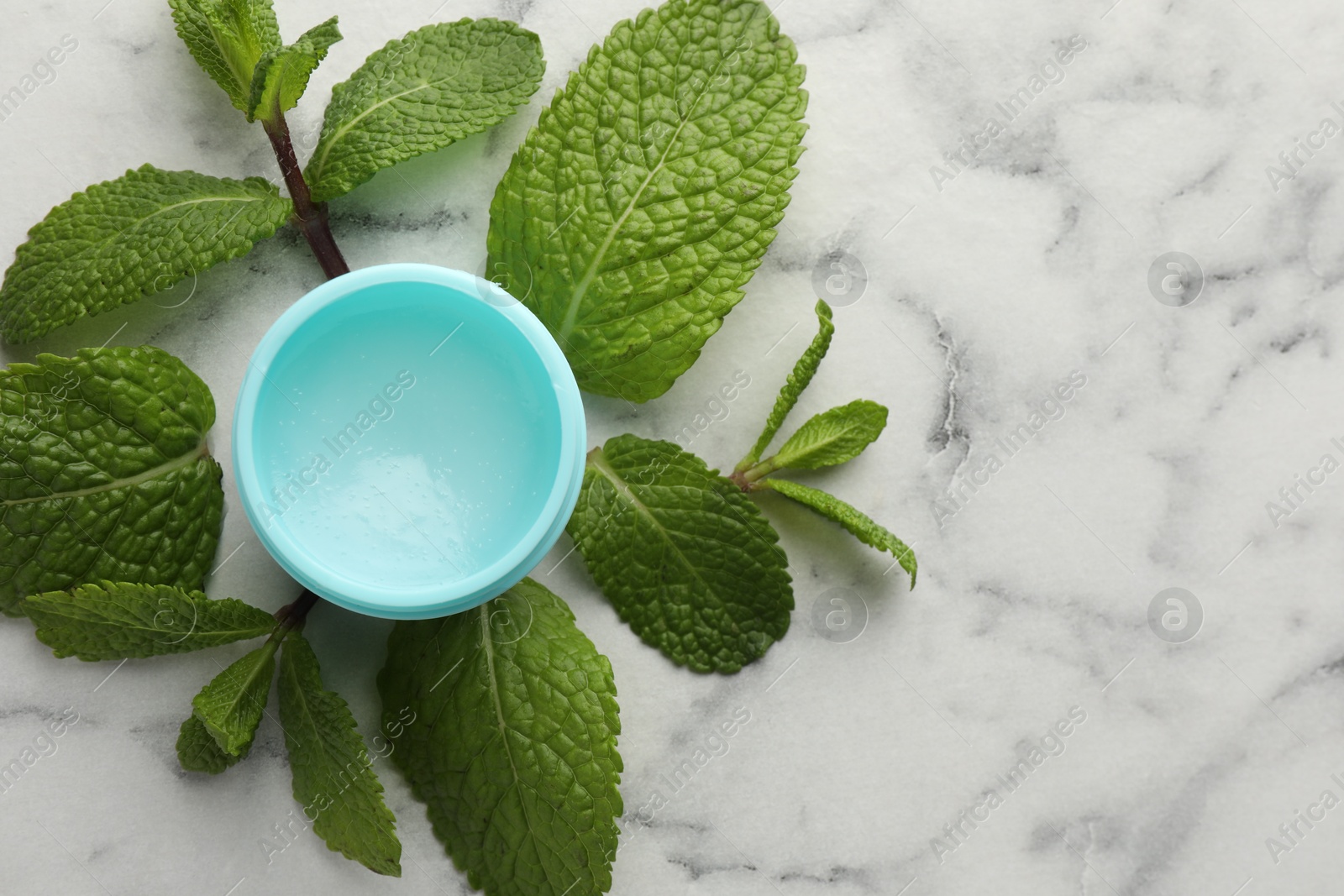 Photo of Mint lip balm and green leaves on white marble background, top view. Space for text