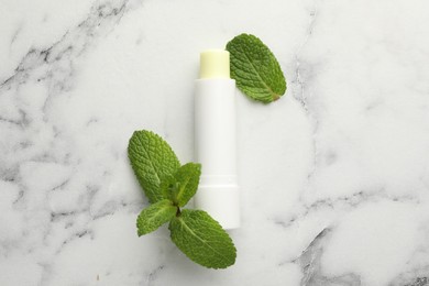 Photo of Mint lip balm and green leaves on white marble table, top view. Cosmetic product