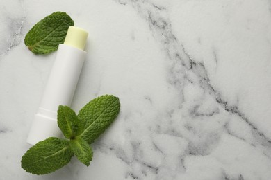 Photo of Mint lip balm and green leaves on white marble background, top view. Space for text