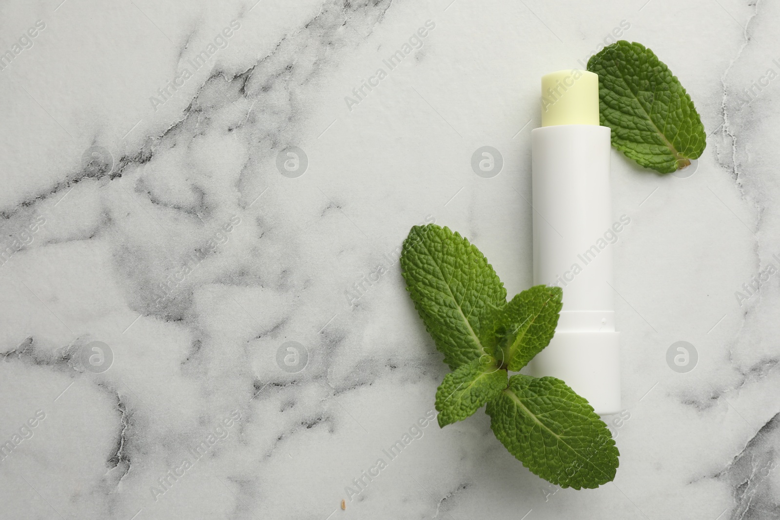 Photo of Mint lip balm and green leaves on white marble background, top view. Space for text