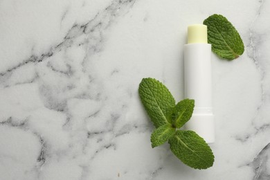 Photo of Mint lip balm and green leaves on white marble background, top view. Space for text