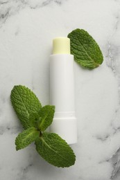 Photo of Mint lip balm and green leaves on white marble table, top view. Cosmetic product