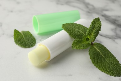 Photo of Mint lip balm and green leaves on white marble table, closeup. Cosmetic product