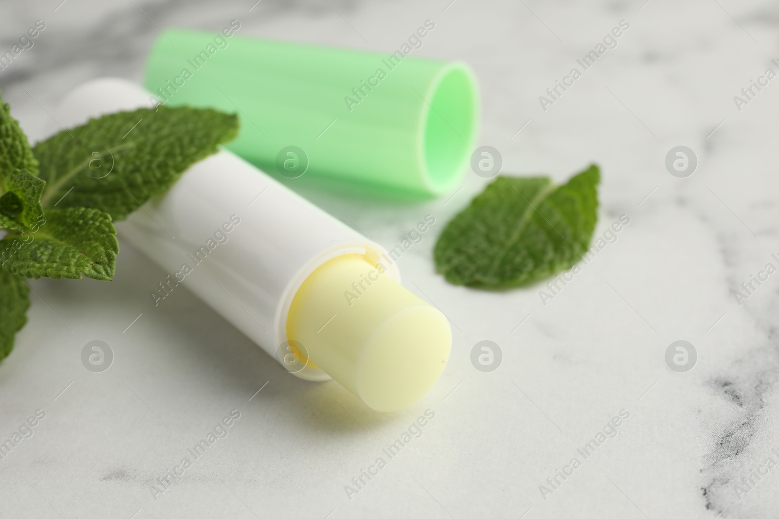 Photo of Mint lip balm and green leaves on white marble table, closeup. Cosmetic product