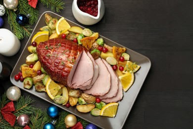 Photo of Tasty baked ham served with vegetables and oranges on black wooden table, flat lay