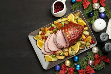 Photo of Tasty baked ham served with vegetables and oranges on black wooden table, flat lay