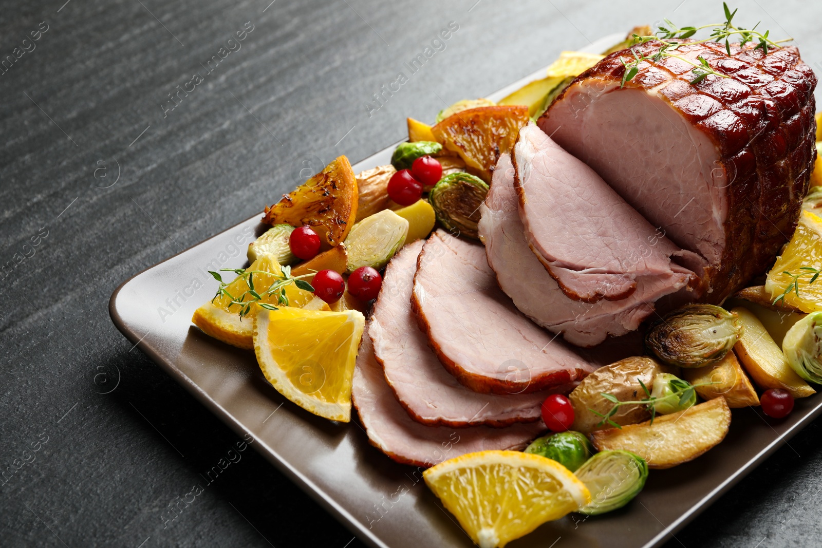 Photo of Tasty baked ham served with vegetables and oranges on black table